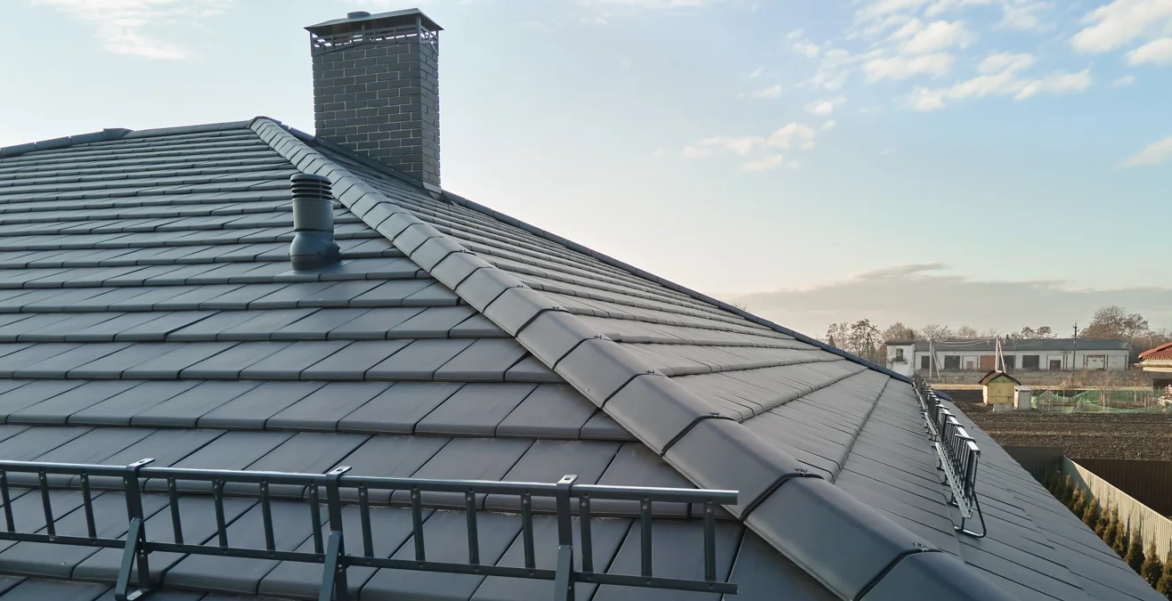 Grey tiled house roof with ridge tiles, a chimney and a roof vent